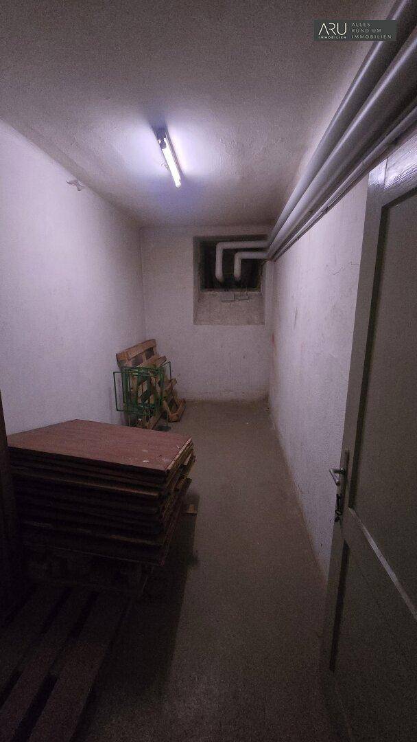 Schmaler Kellerraum mit gestapelten Holzplatten und einem kleinen Fenster, ideal zur Lagerung.