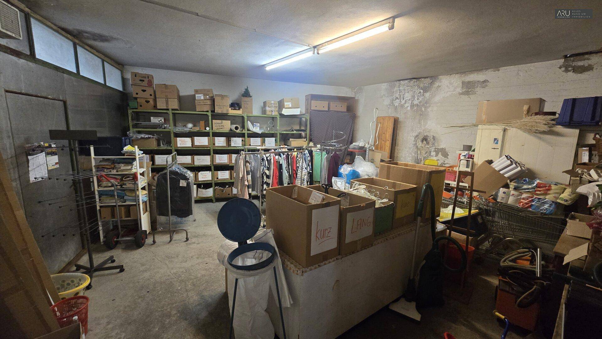 Großer, unaufgeräumter Kellerraum mit Regalen, Kleiderständern und vielen Lagerboxen.