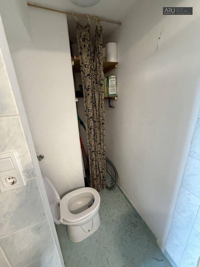 Kleines WC mit einfacher Toilette und Stauraum hinter einem Vorhang.