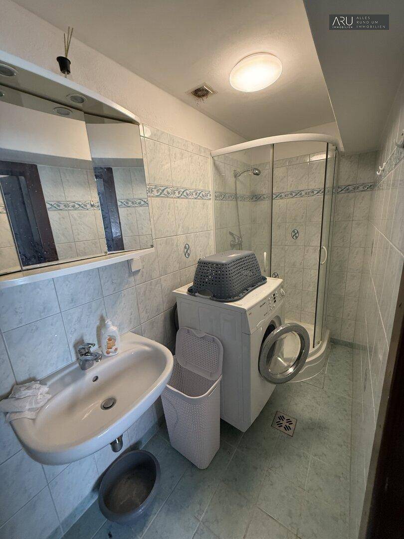 Gefliestes Badezimmer mit Dusche, Waschbecken und integrierter Waschmaschine.