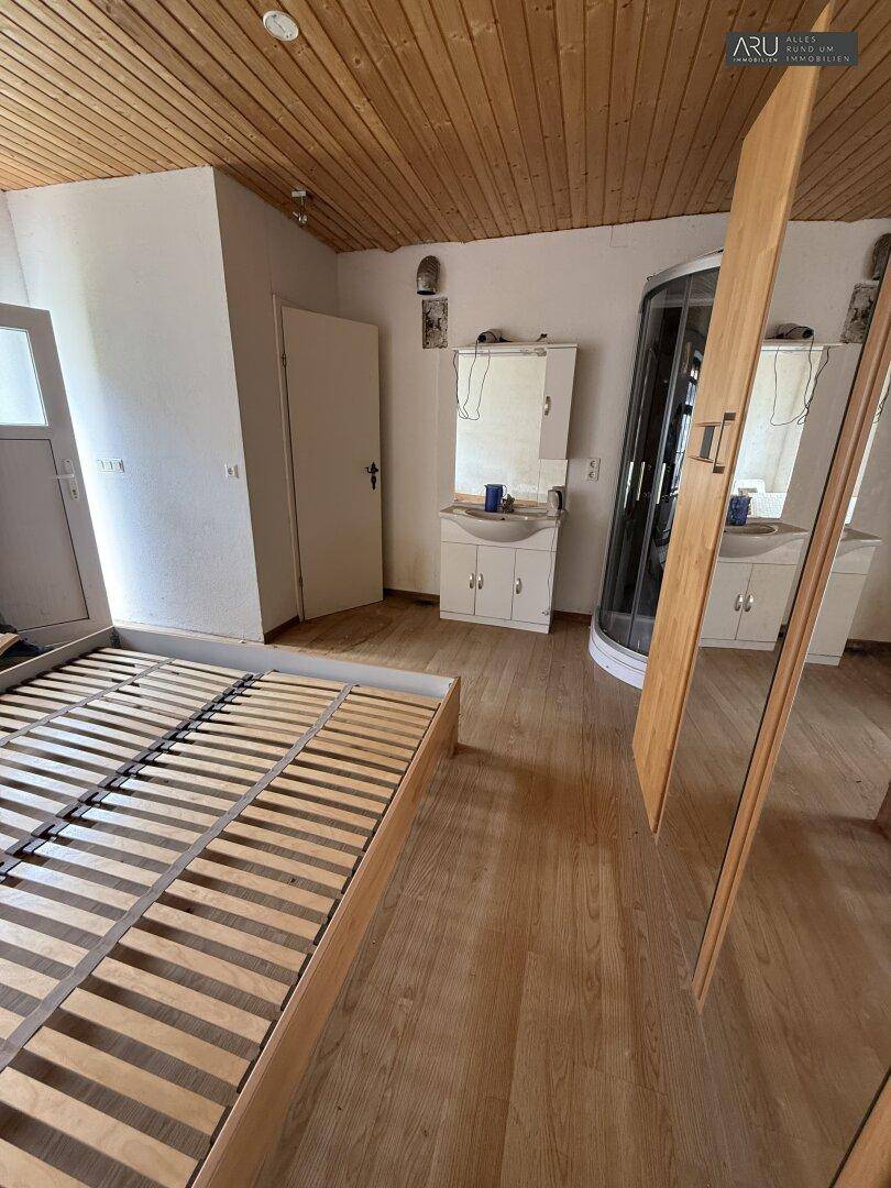 Schlafzimmer mit Holzboden, Holzdecke und offenem Badbereich mit Duschkabine.