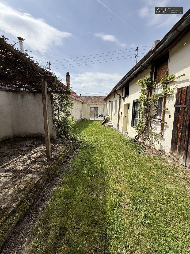 Langer, schmaler Gartenbereich mit Rasen und überdachtem Sitzplatz im Hintergrund.
