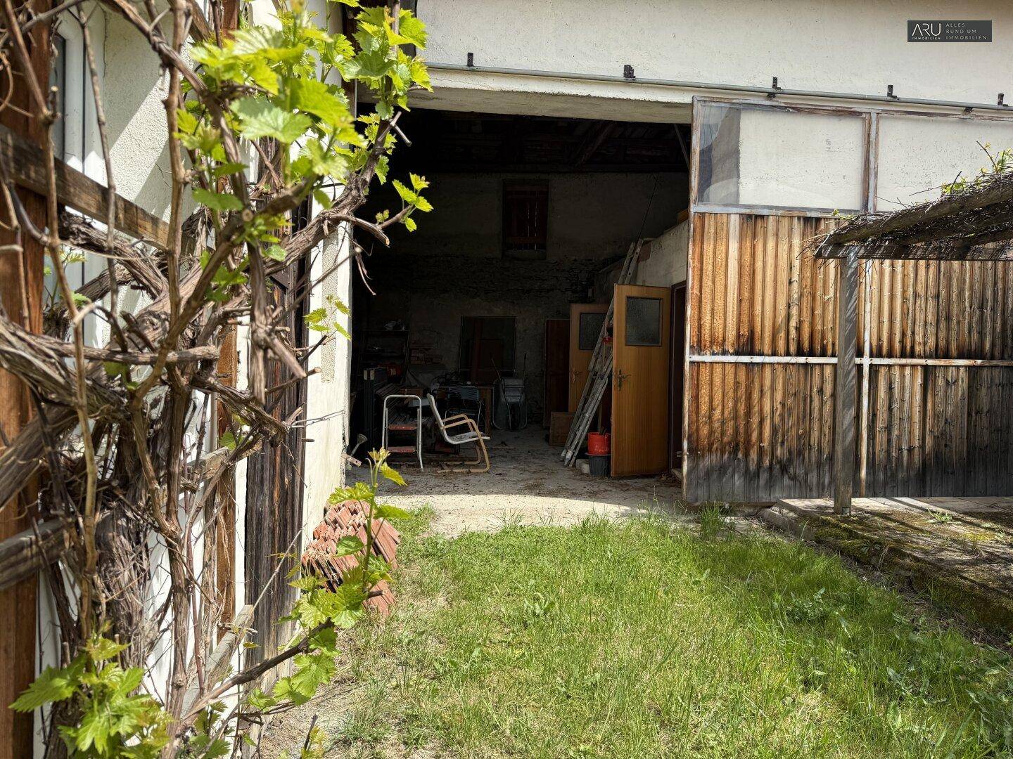 Offene Scheune oder Garage mit Holztoren und Blick auf den Innenhof.