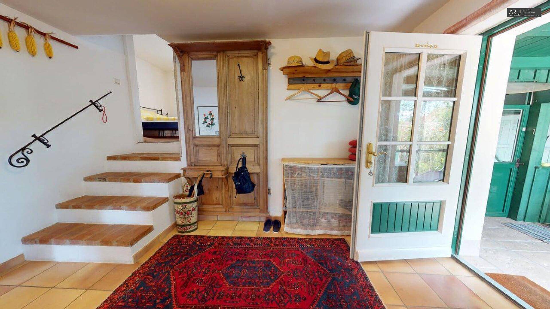 Eingangsbereich mit Terrakotta-Fliesenboden, Holzmöbeln und Treppe zum Obergeschoss, sehr einladend.