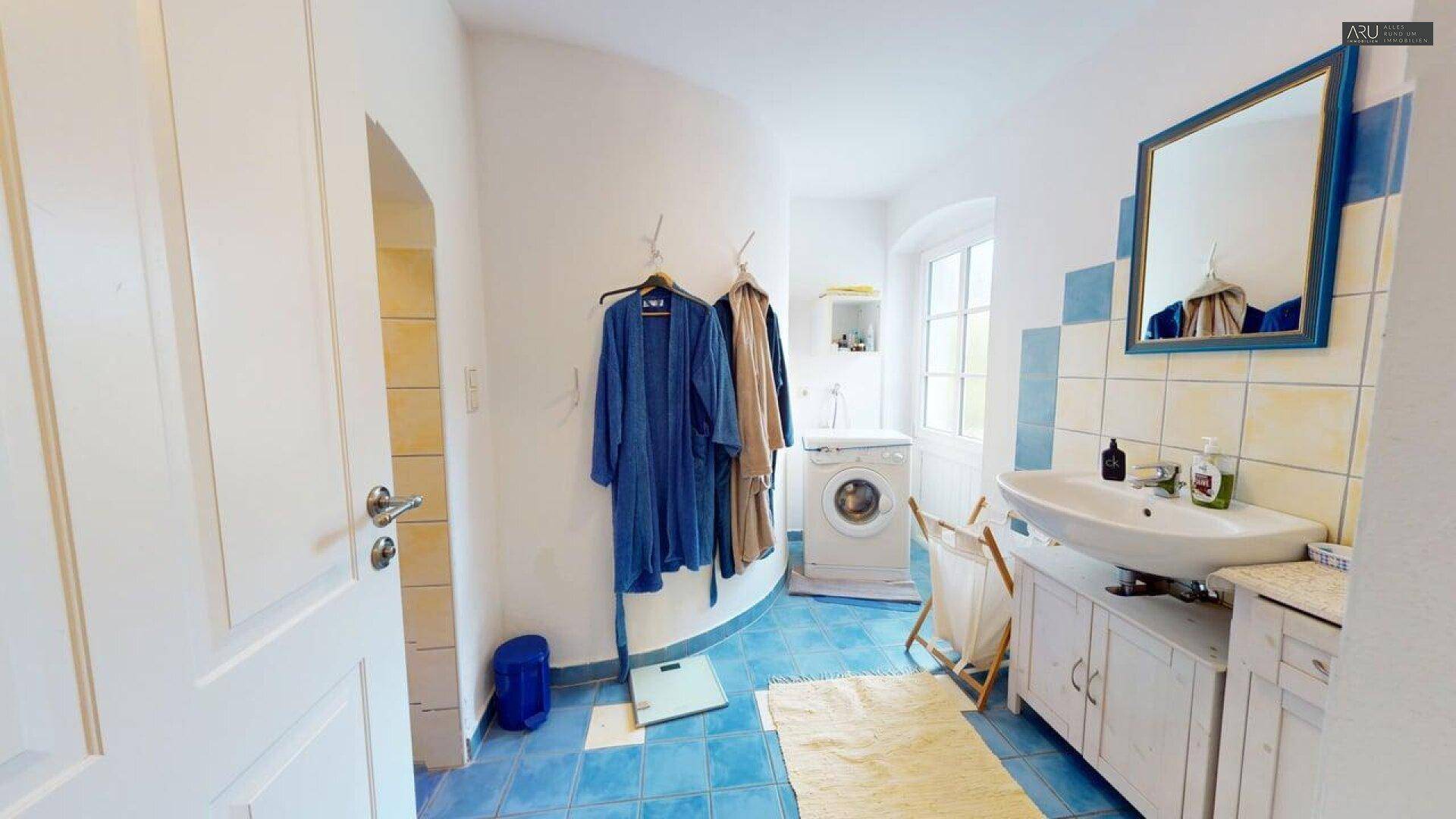 Badezimmer mit Waschbecken, Waschmaschine und blauen Fliesen, hell und praktisch ausgestattet.