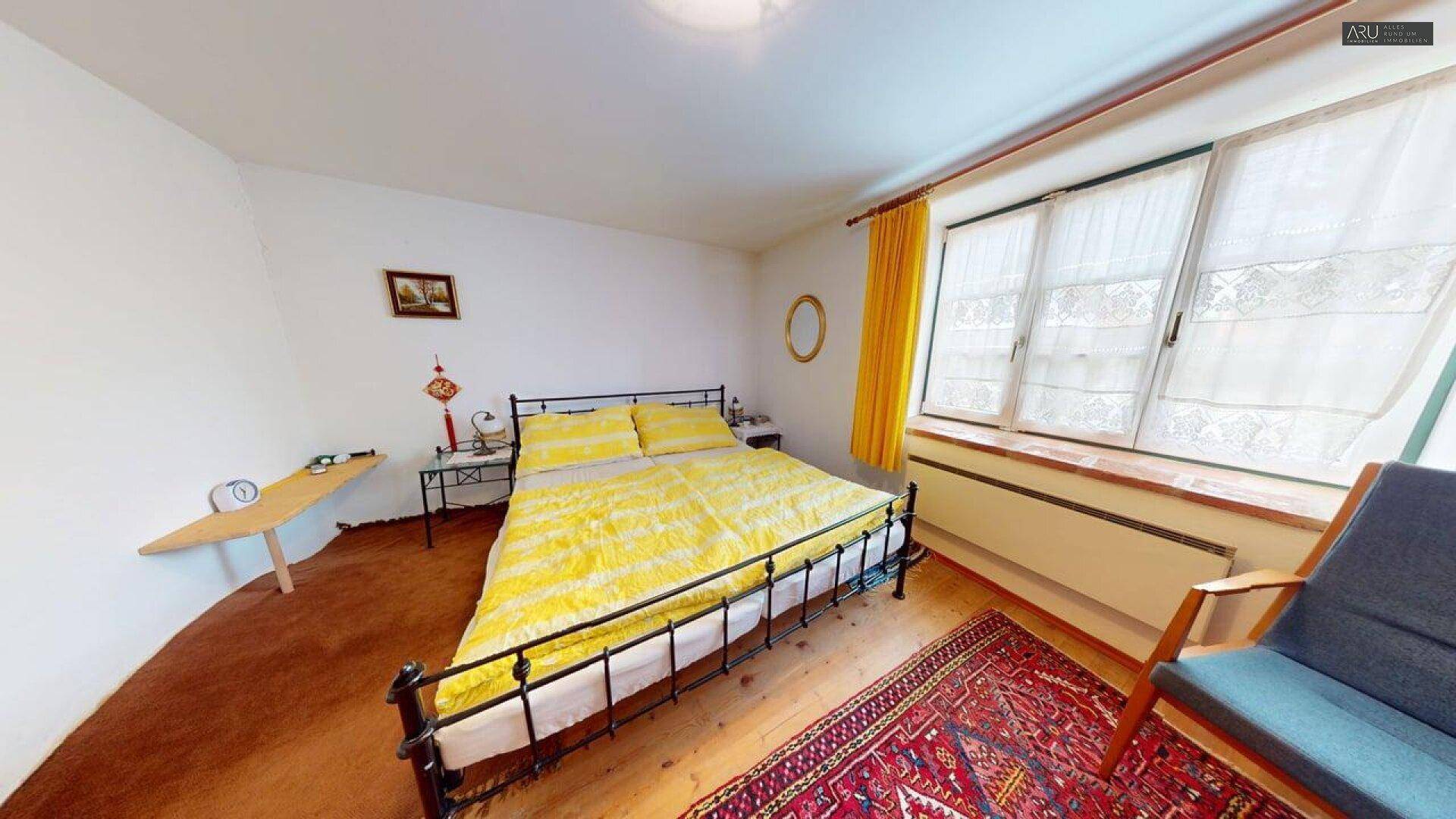 Schlafzimmer mit Doppelbett, Holzboden und gelben Akzenten, hell und freundlich gestaltet.