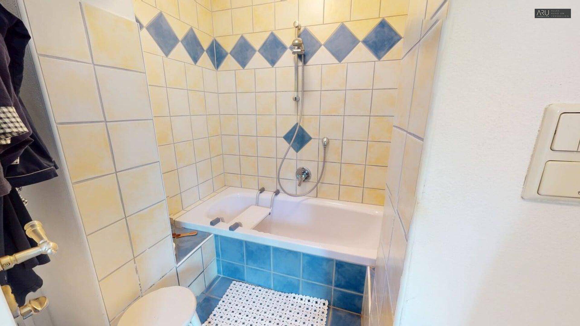 Badezimmer mit Badewanne und Duschfunktion, gefliest in Gelb und Blau, funktional und hell.