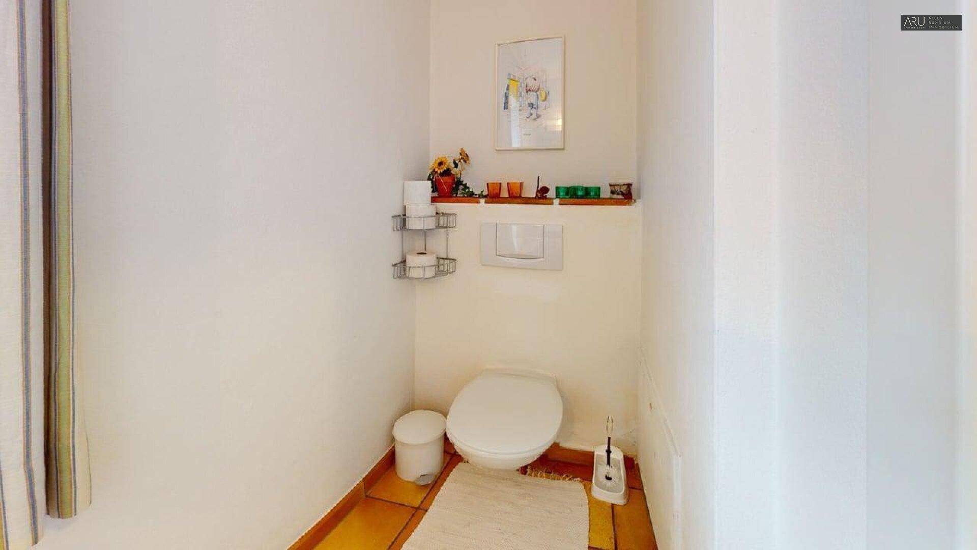 Separates WC mit Wand-WC und Terrakotta-Fliesenboden, einfach und funktional eingerichtet.