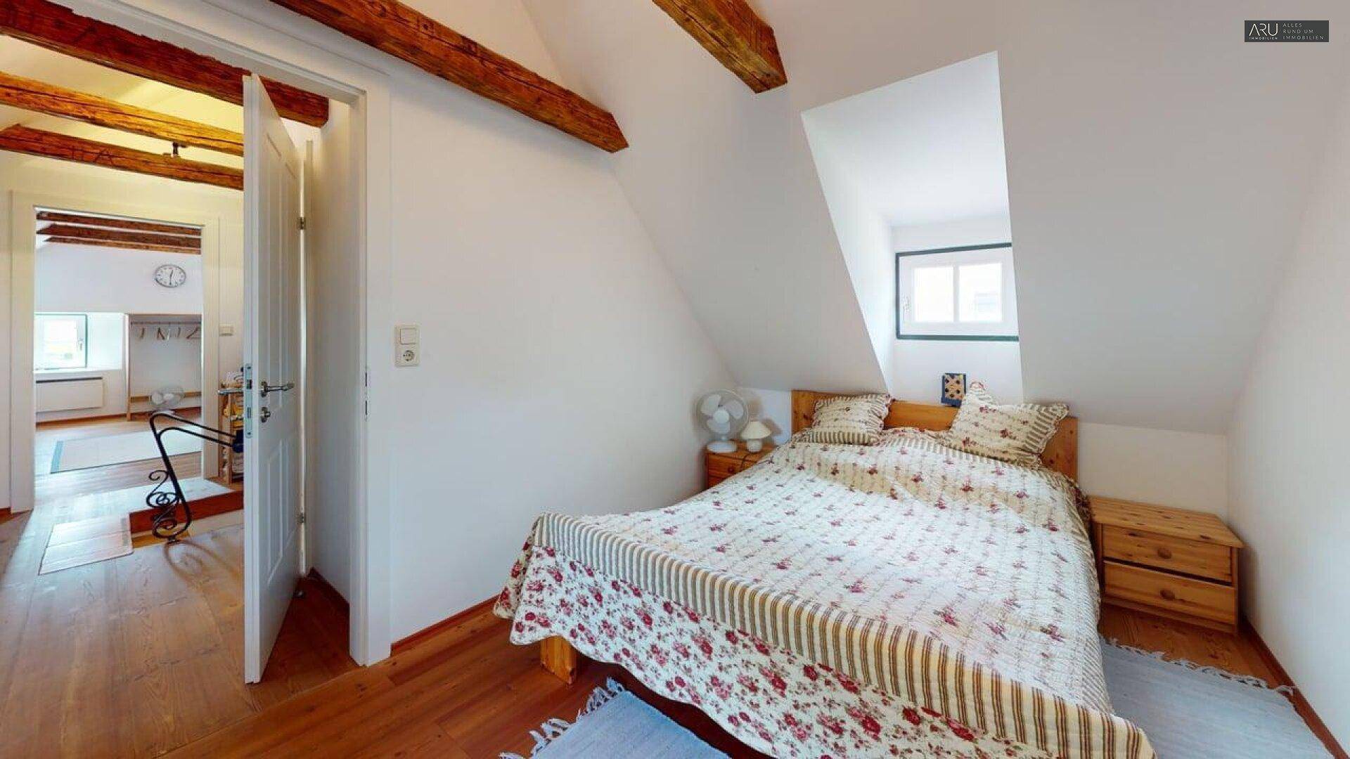 Gemütliches Dachgeschoss-Schlafzimmer mit Holzbalken, Holzboden und Dachfenster, sehr einladend.