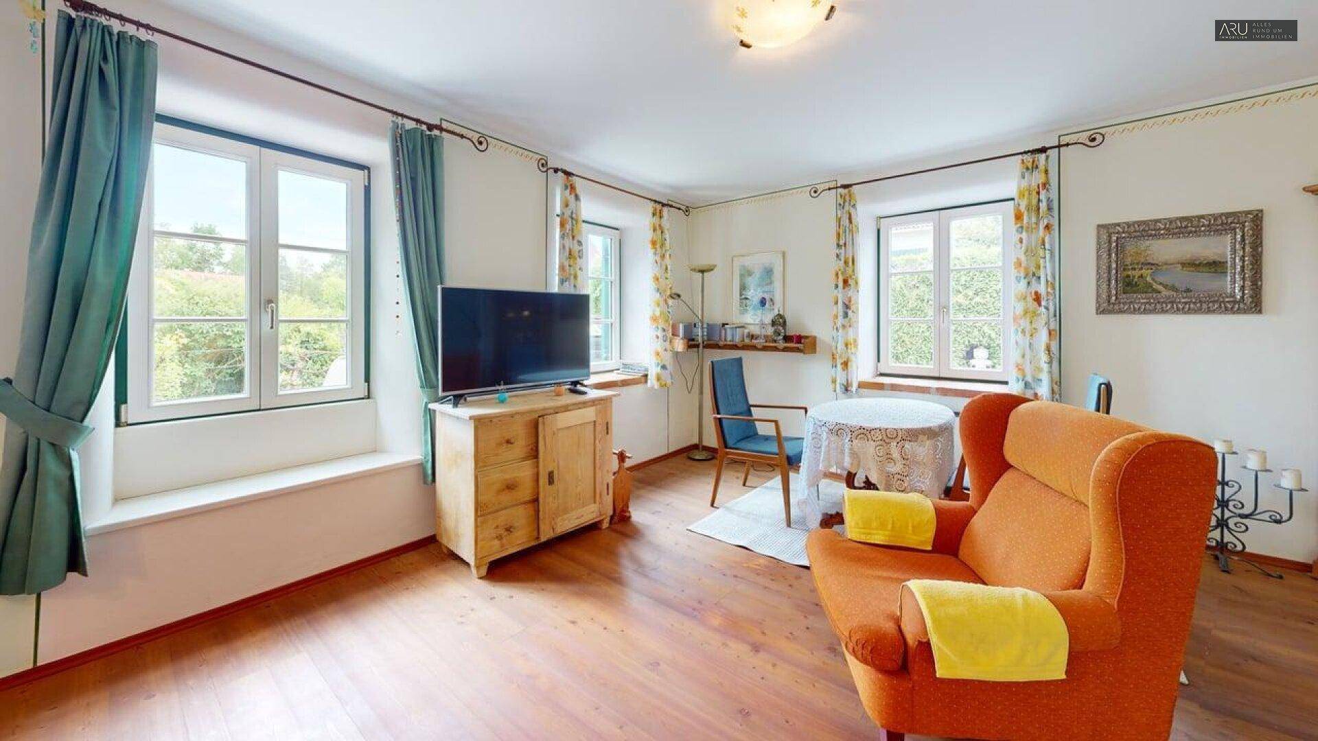 Heller Wohnbereich mit Holzboden, großen Fenstern und traditioneller Einrichtung, bietet viel Tageslicht.