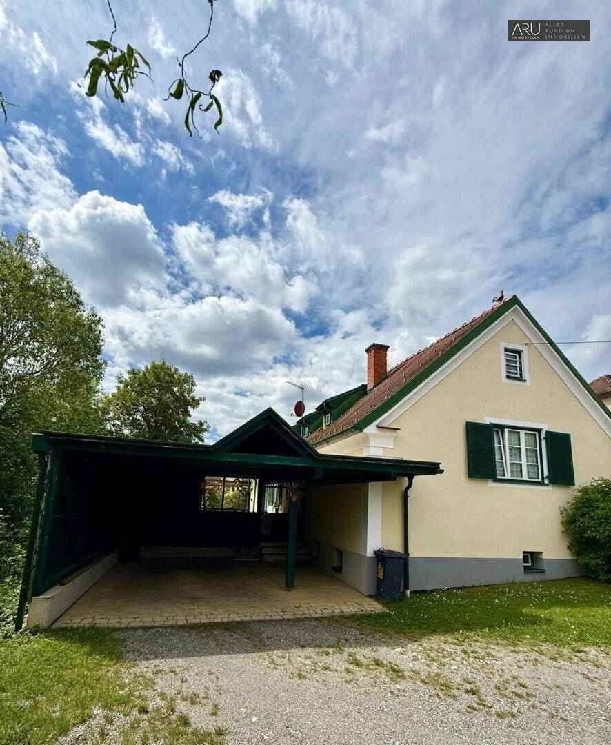 Hausfassade mit Carport und grünem Dach, bietet geschützten Parkplatz für Fahrzeuge.