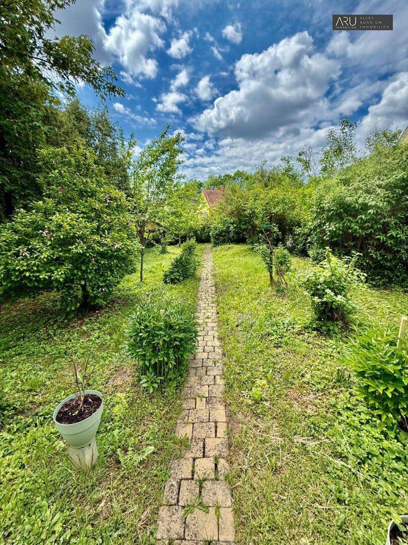 Naturbelassener Garten mit Steinweg, üppiger Vegetation und viel Grünfläche, sehr idyllisch.