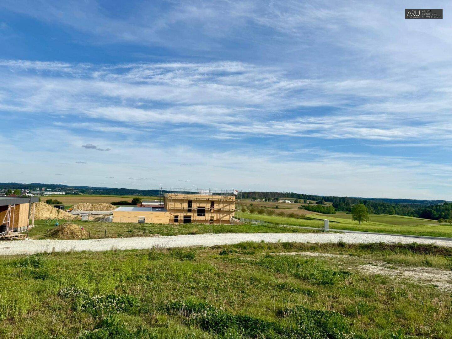 Baustelle eines neuen Hauses mit Holzrahmenbauweise, umgeben von grünen Feldern und Natur.