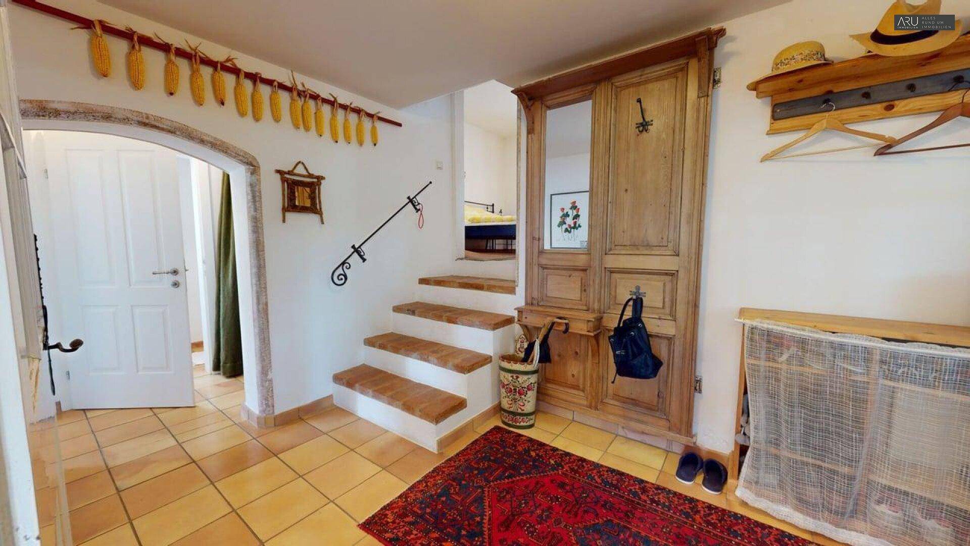 Heller Eingangsbereich mit Holztreppe, rustikaler Garderobe und warmen Terrakotta-Fliesenboden.