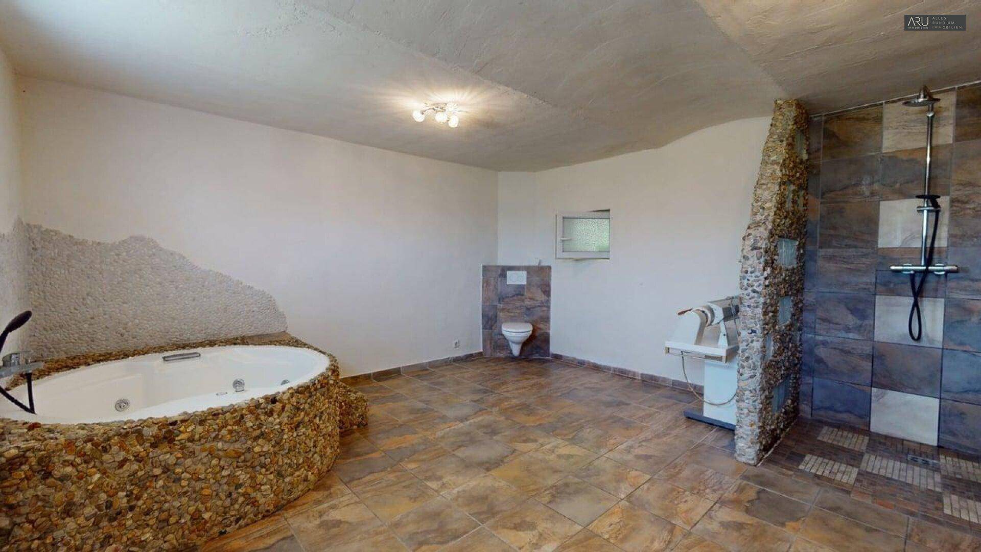 Großes Badezimmer mit Whirlpool, Steindekor und begehbarer Dusche.