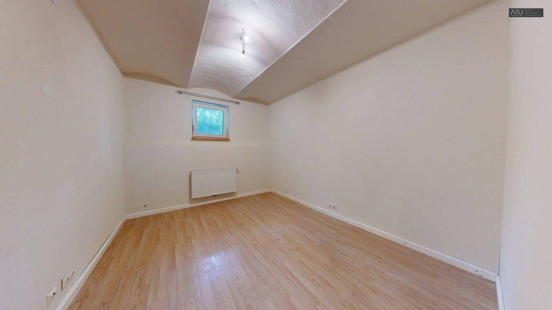 Einfaches Zimmer mit Holzboden und kleinerem Fenster, ideal als Gästezimmer.