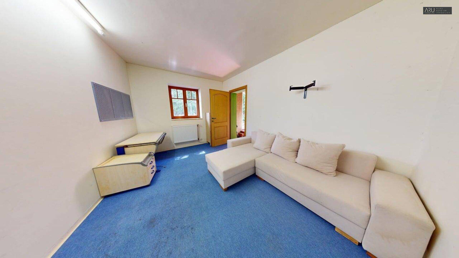Gemütliches Wohnzimmer mit Sofa, Schreibtisch und blauem Teppichboden.