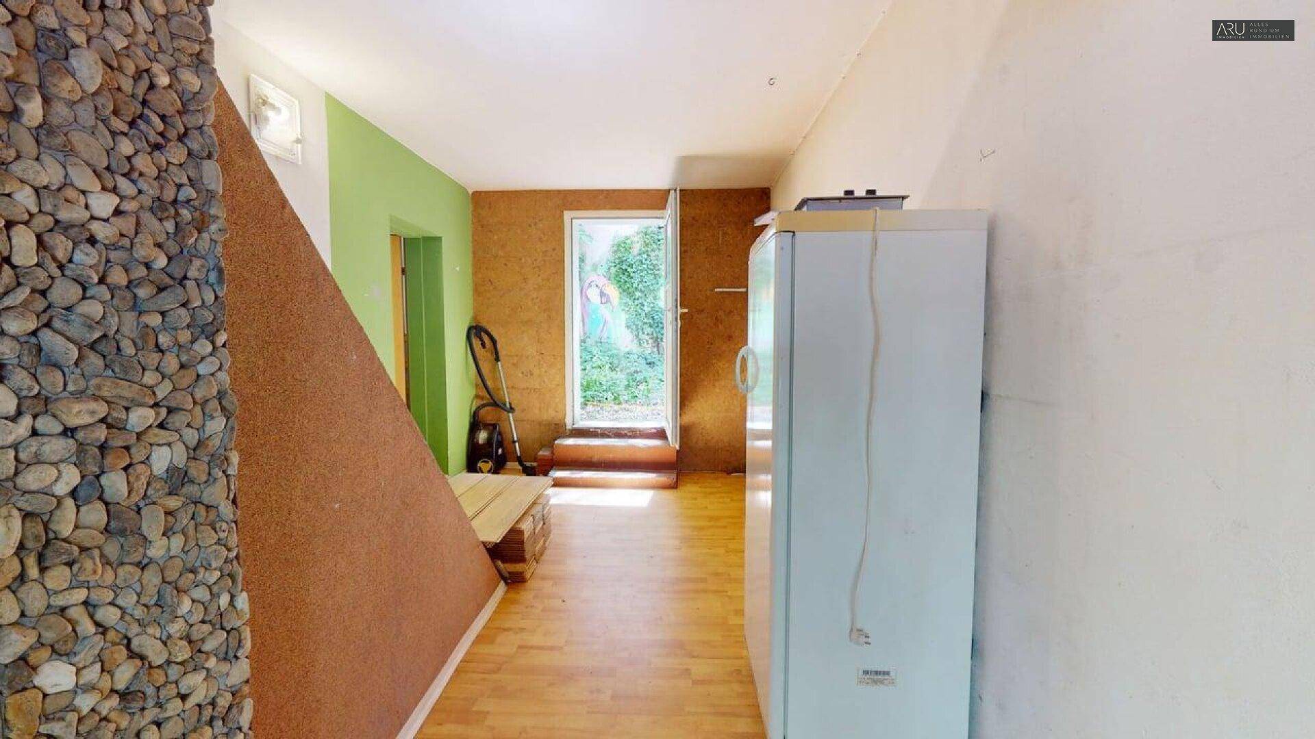 Eingangsbereich mit rustikaler Steinwand, Kühlschrank und Zugang zum Garten.