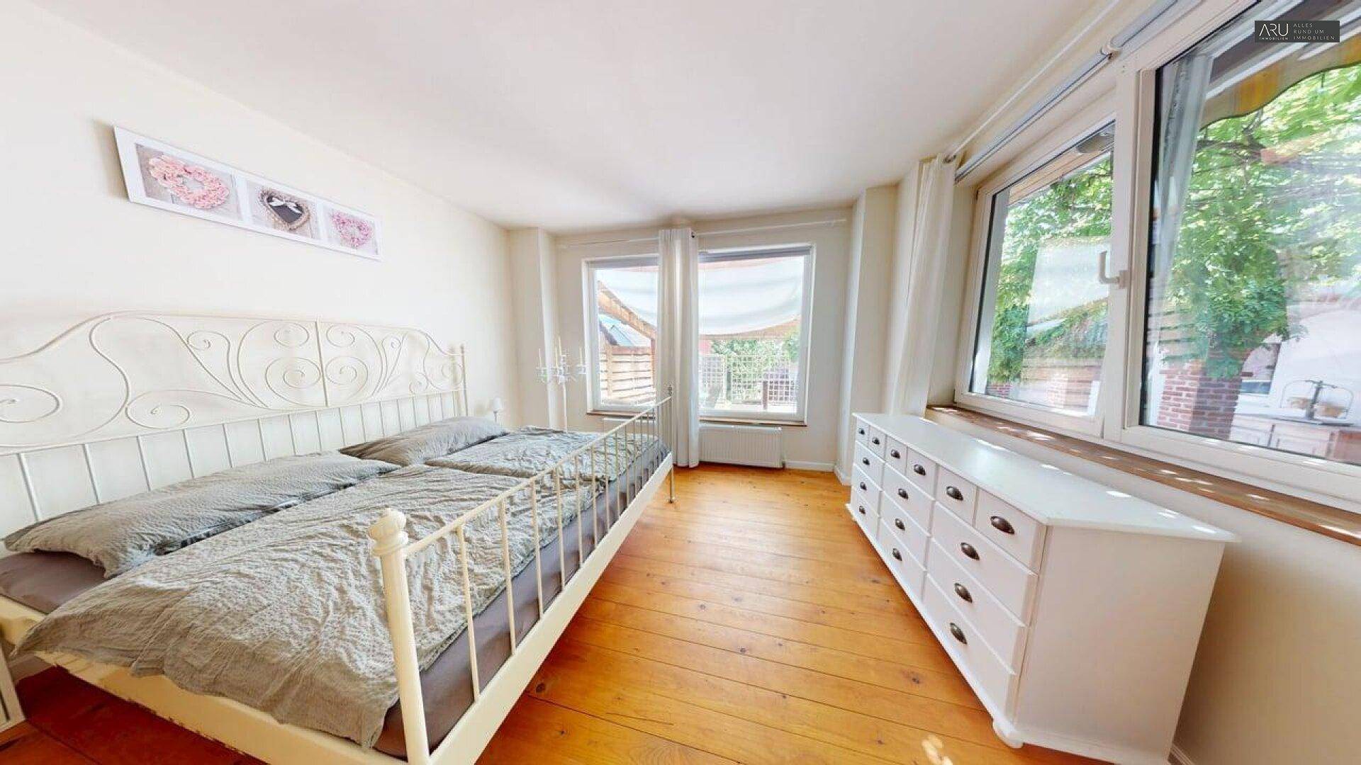 Helles Schlafzimmer mit Holzboden, schmiedeeisernem Bett und Blick ins Grüne.