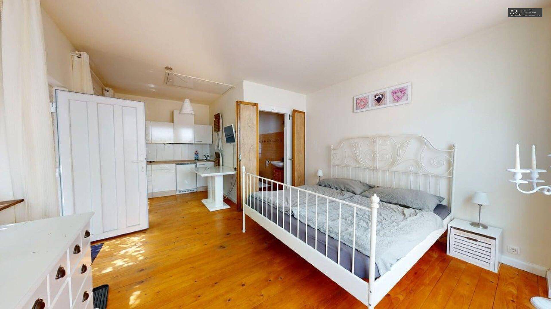 Schlafzimmer mit Holzboden, schmiedeeisernem Bett und integrierter Küchenzeile.