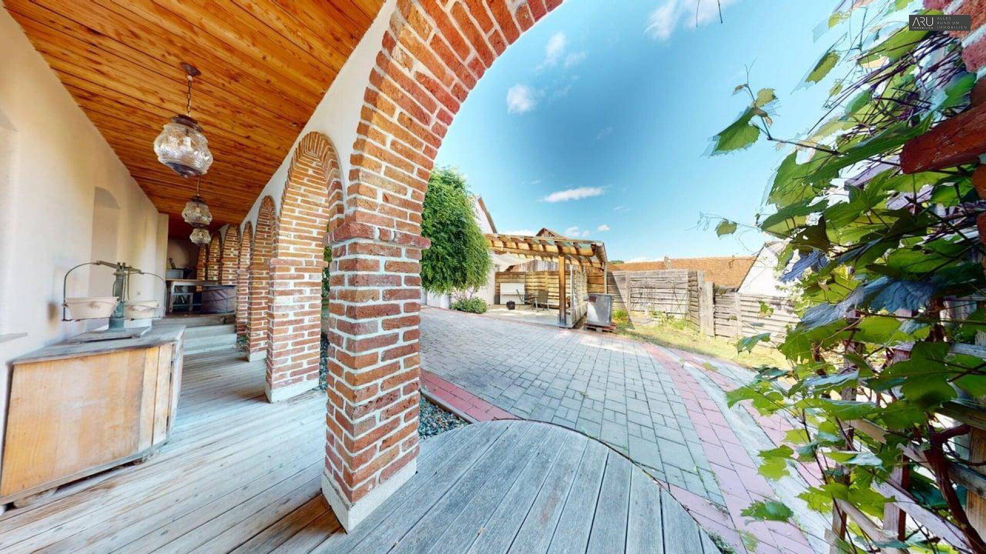 Historischer Innenhof mit Ziegelbögen, Holzboden und Blick auf den Garten.