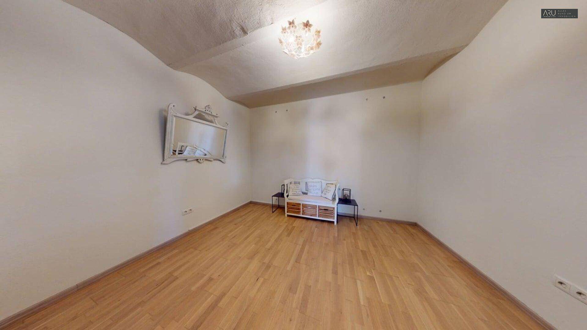 Geräumiges Zimmer mit Holzboden, dekorativem Spiegel und indirekter Beleuchtung.
