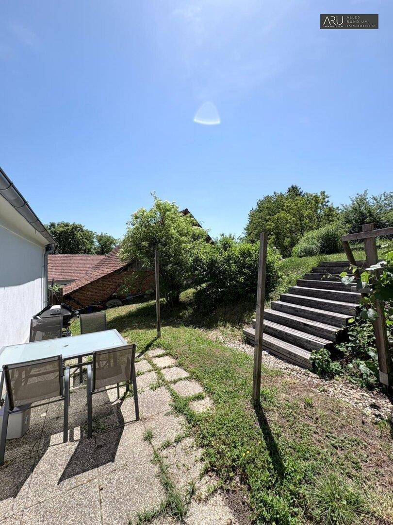Sitzbereich im Garten mit Steinfliesen und Holztreppe zu einer oberen Ebene.