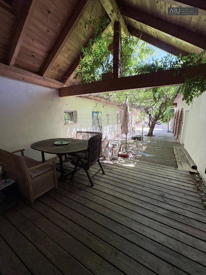 Überdachte Holzterrasse mit Gartenmöbeln und Blick ins Grüne.
