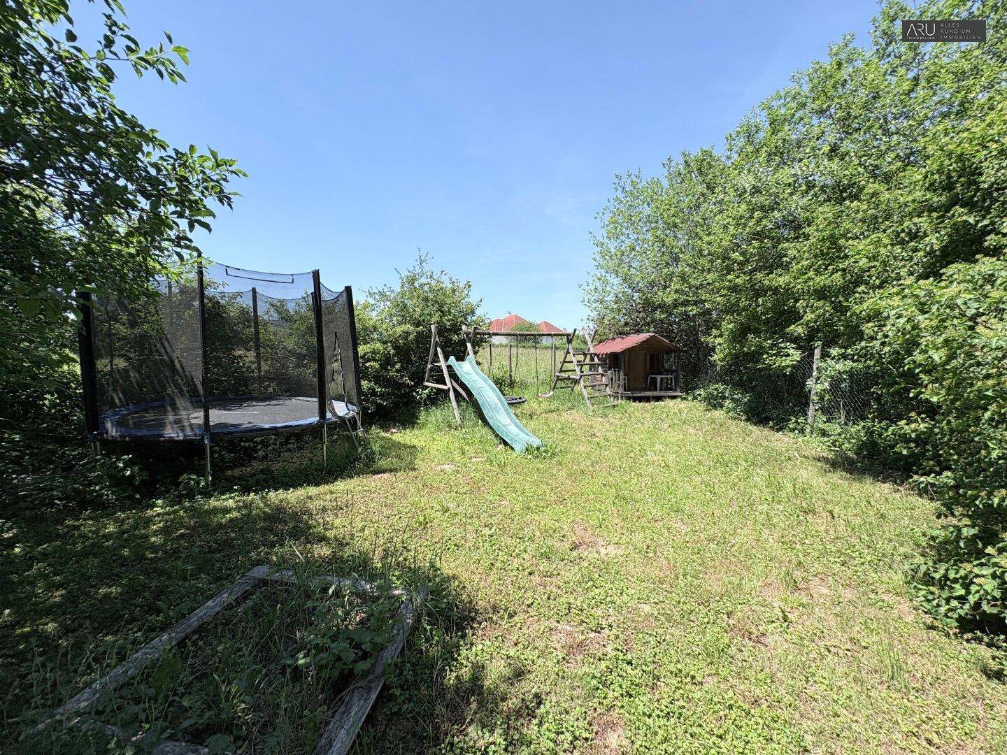 Sonniger Garten mit Trampolin, Rutsche und Spielhaus für Kinder.