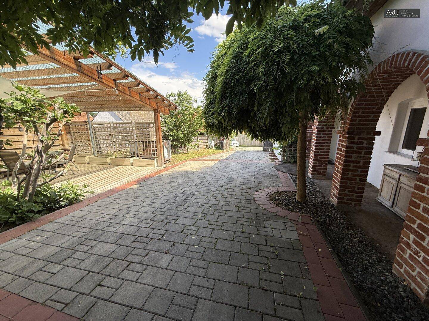 Gepflasterter Weg führt zu einem überdachten Bereich mit Holzpergola und Garten.