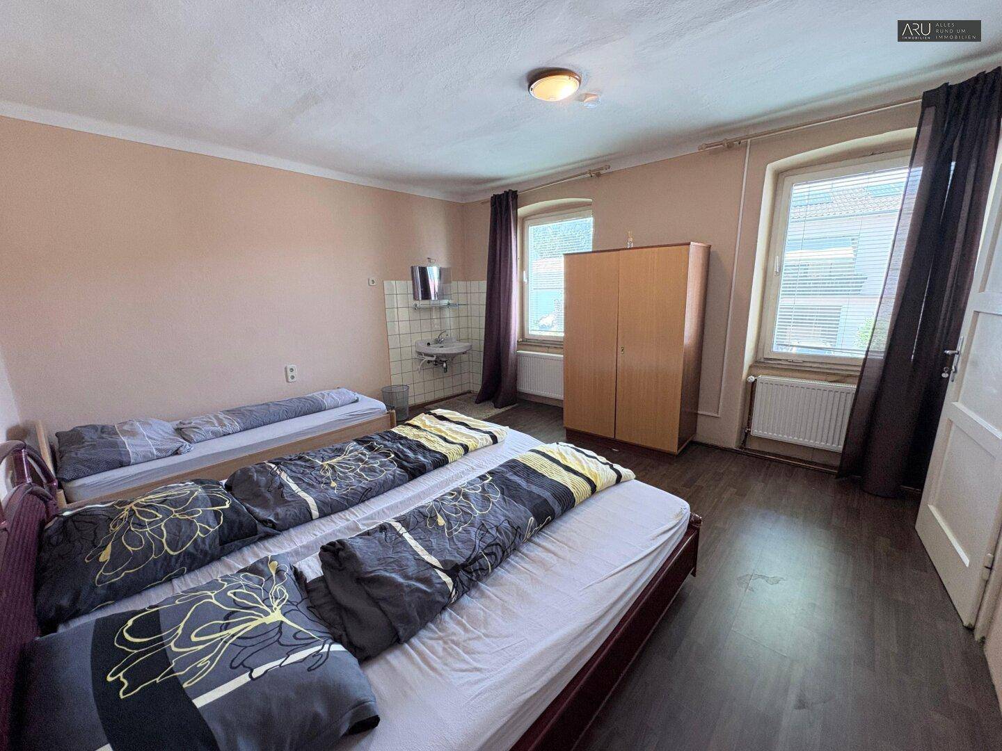 Schlafzimmer mit zwei Betten, einem Kleiderschrank und einem kleinen Waschbecken im Raum.
