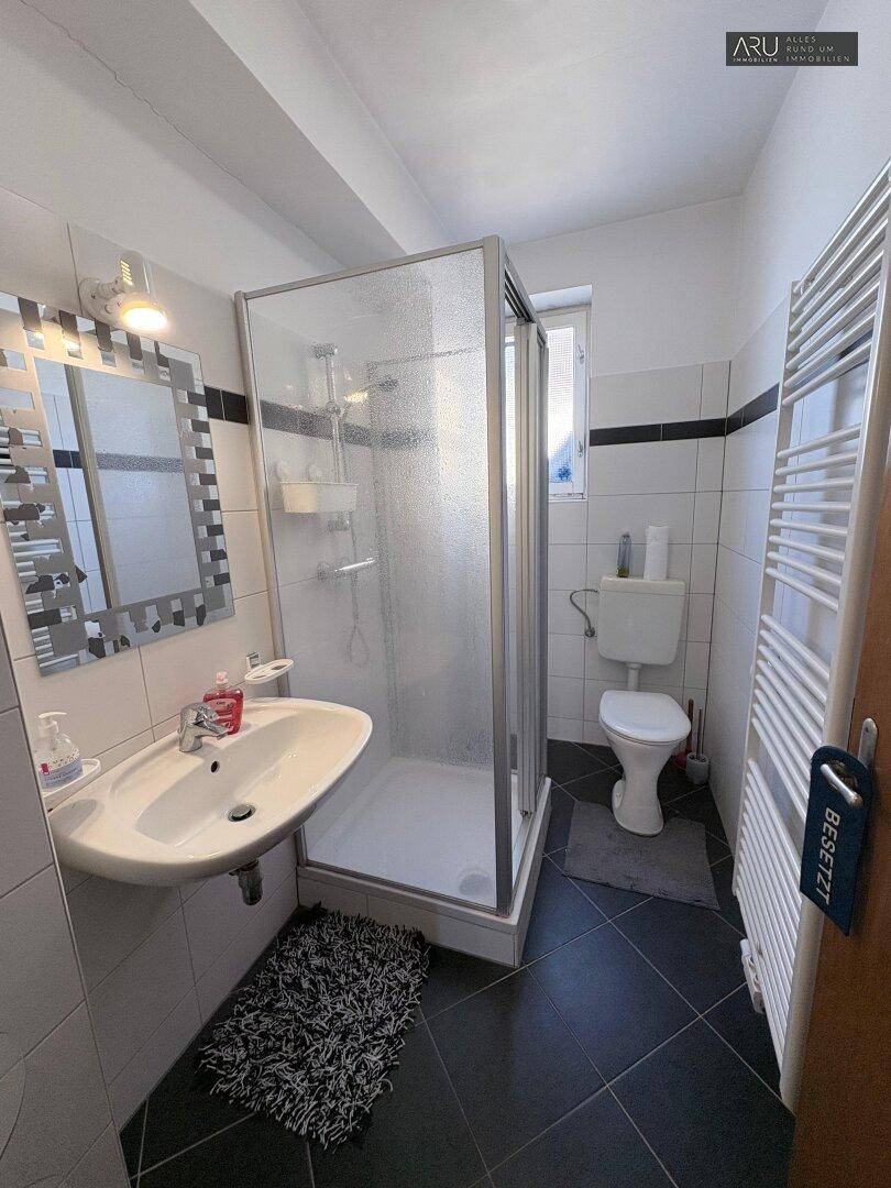 Modernes Badezimmer mit Duschkabine, Toilette, Waschbecken und beheiztem Handtuchhalter.