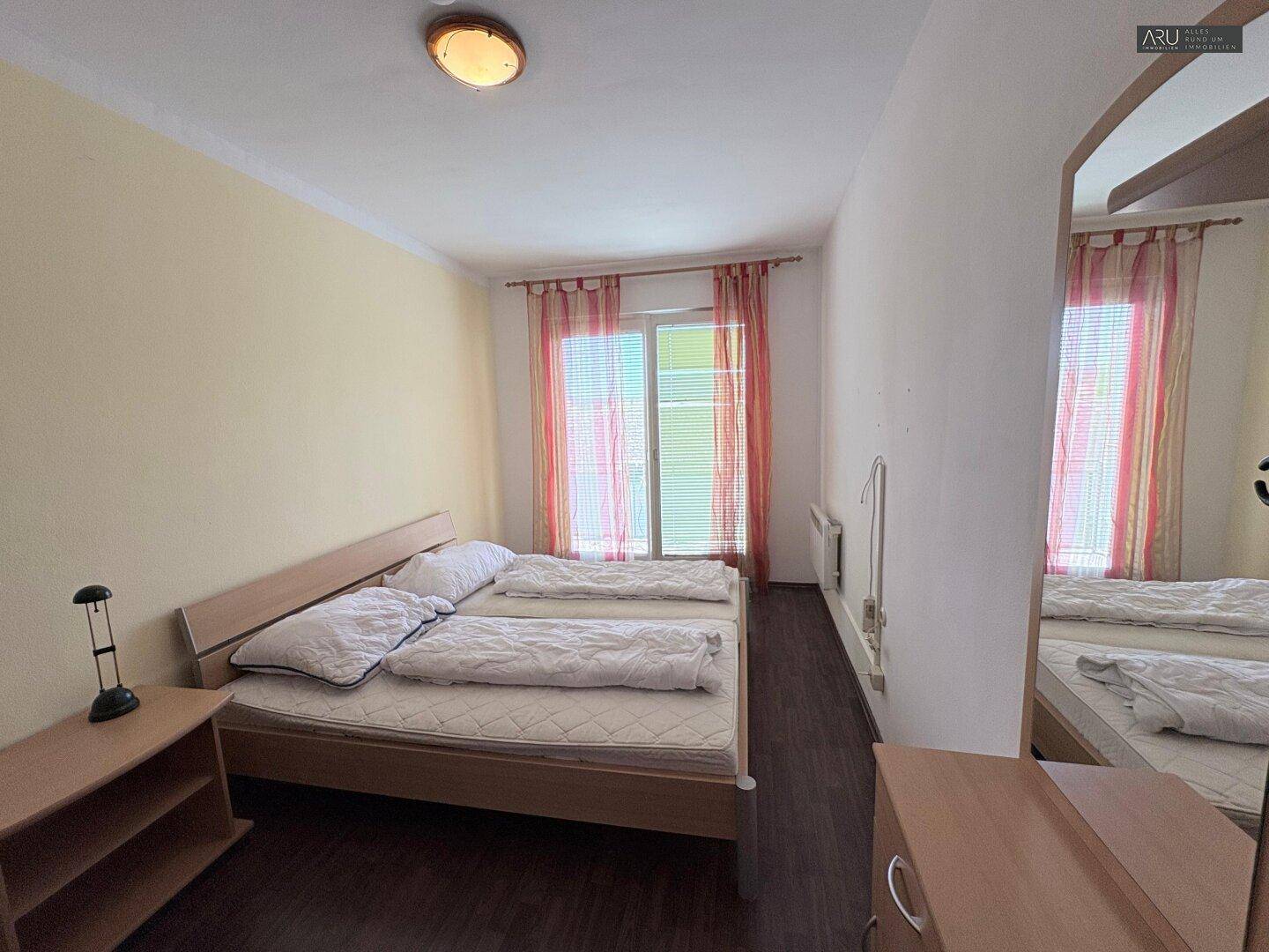 Schlafzimmer mit Doppelbett und einem großen Spiegel, der den Raum optisch erweitert.