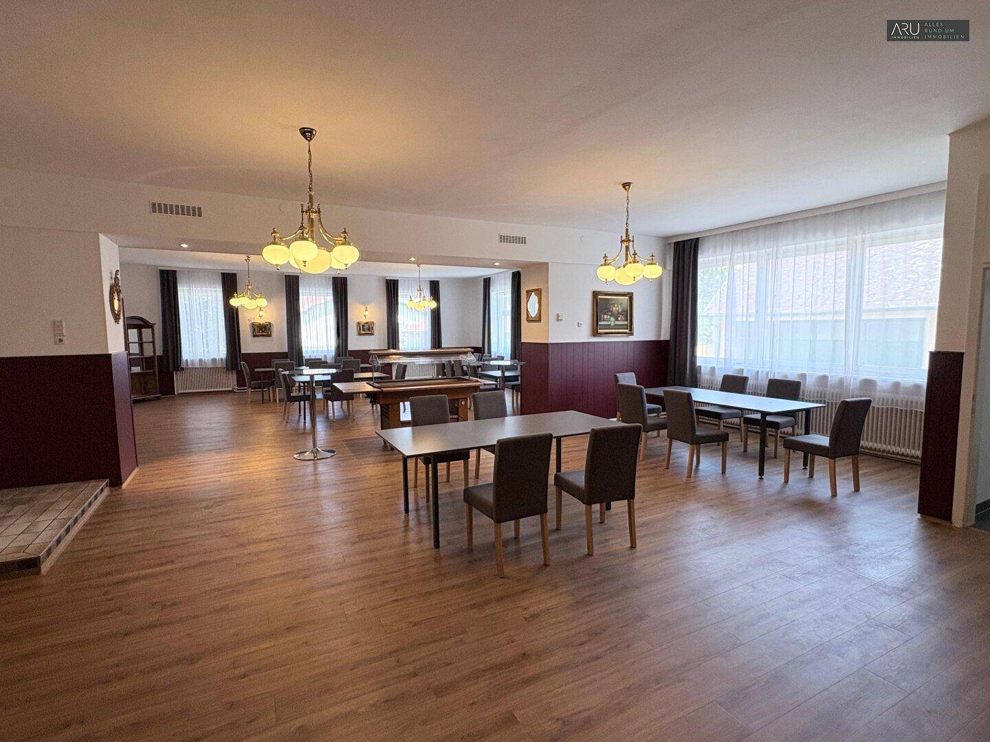 Großer Speisesaal mit Holzboden, vielen Tischen und Stühlen sowie klassischen Kronleuchtern.