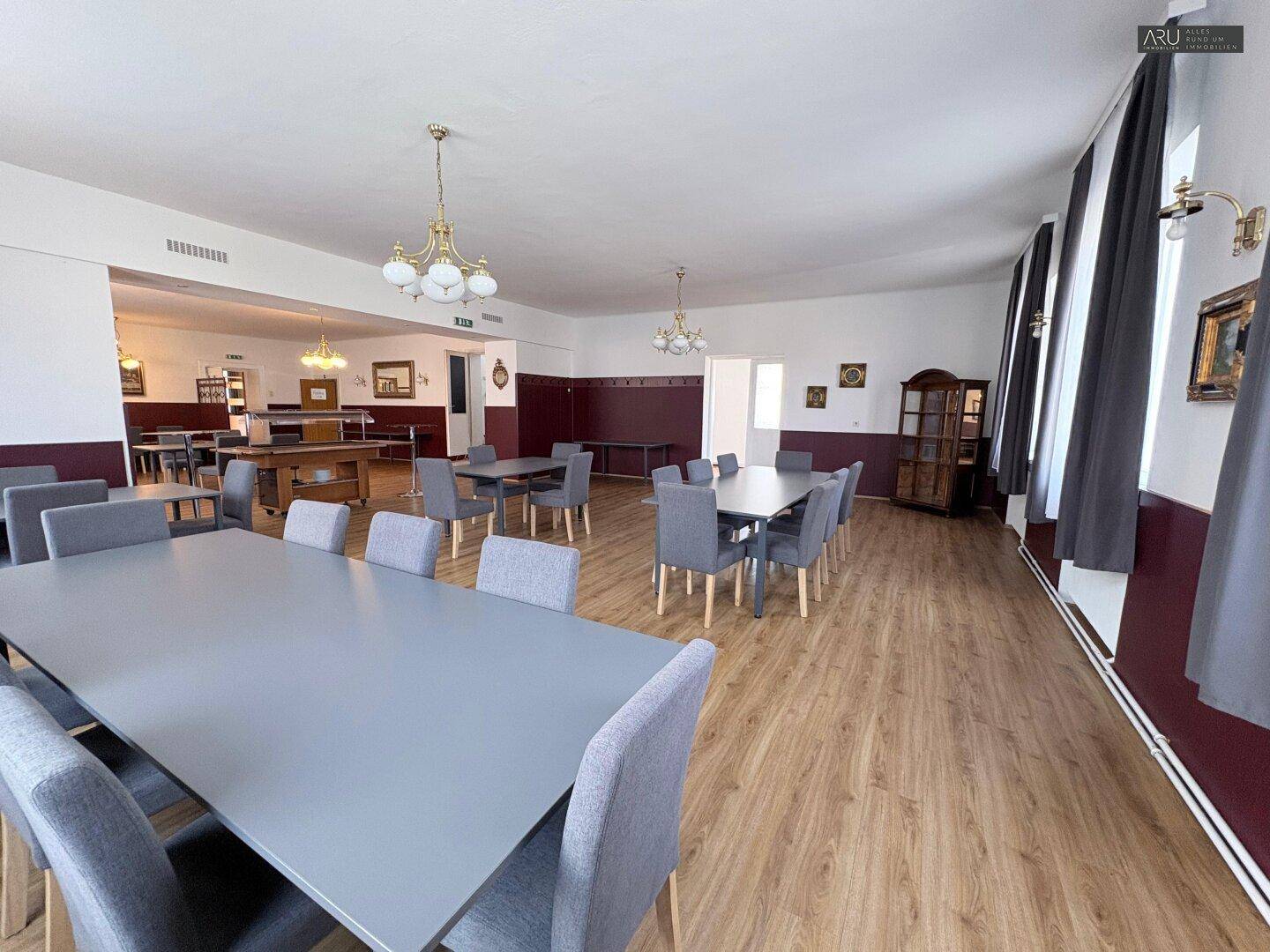 Weiterer Blick in den geräumigen Speisesaal mit zahlreichen Sitzgelegenheiten und großen Fenstern.