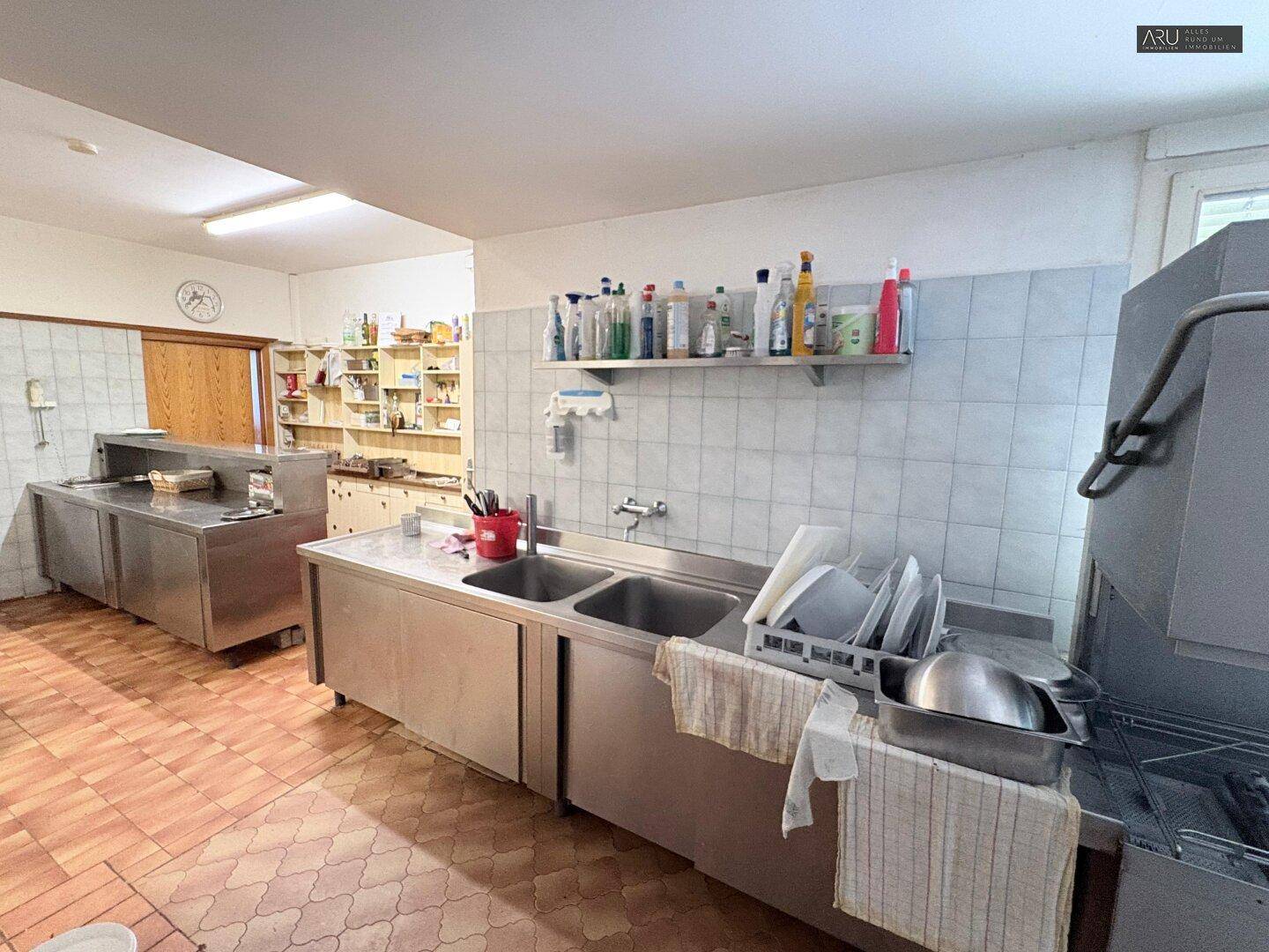 Professionelle Küche mit Edelstahlarbeitsflächen, Spülbecken und gefliesten Wänden für den Gastronomiebetrieb.