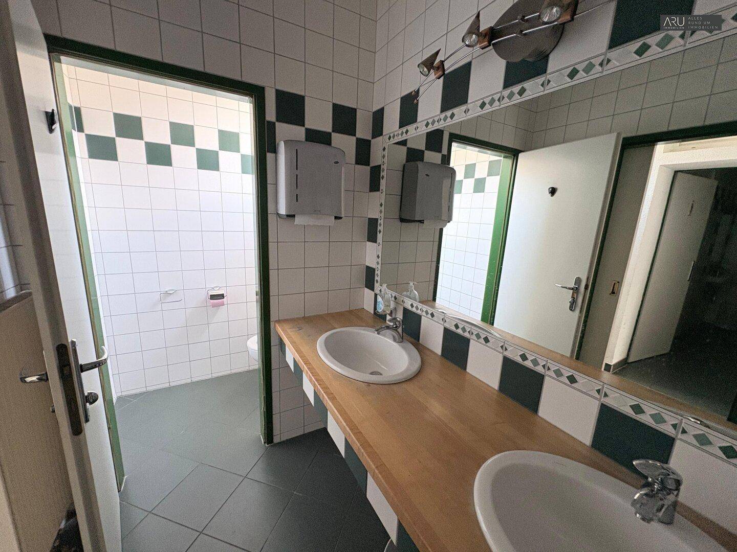Geräumiger Toilettenbereich mit mehreren Waschbecken, großen Spiegeln und gefliesten Wänden.