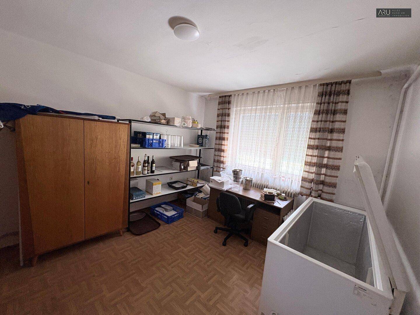 Büro oder Abstellraum mit Schreibtisch, Regalen und einem Gefrierschrank.