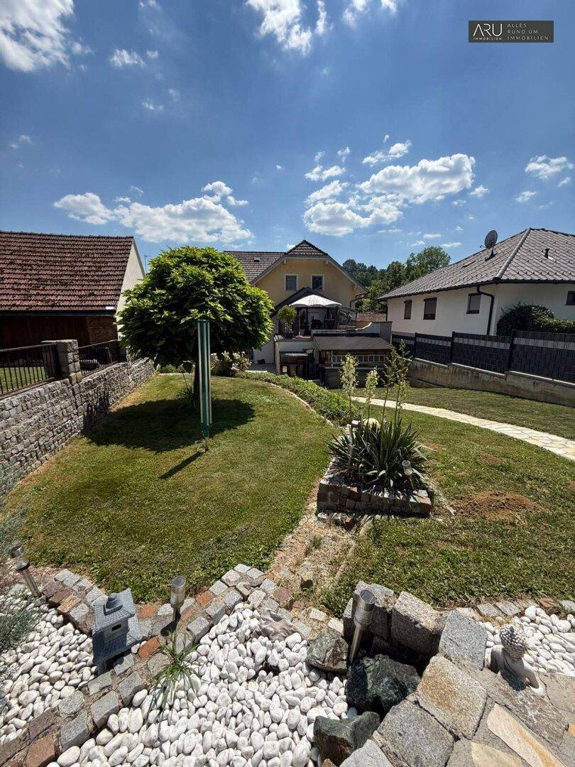 Gepflegter Garten mit Ziersteinen, Rasenflächen und Bäumen.