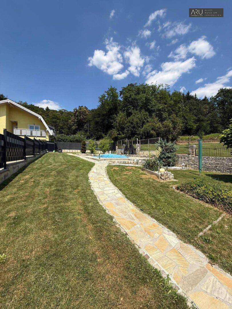 Großer Garten mit Steinweg, Rasenfläche und Pool im Hintergrund.