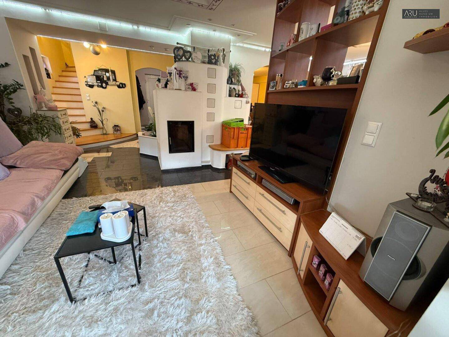 Wohnbereich mit Fernseher, Kamin und Blick auf die Treppe.