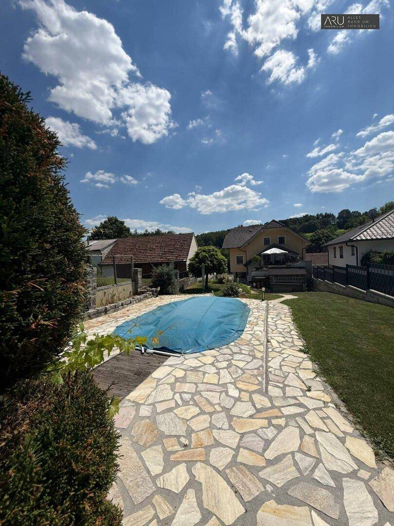 Großer Poolbereich mit Steinplatten und Rasenflächen.