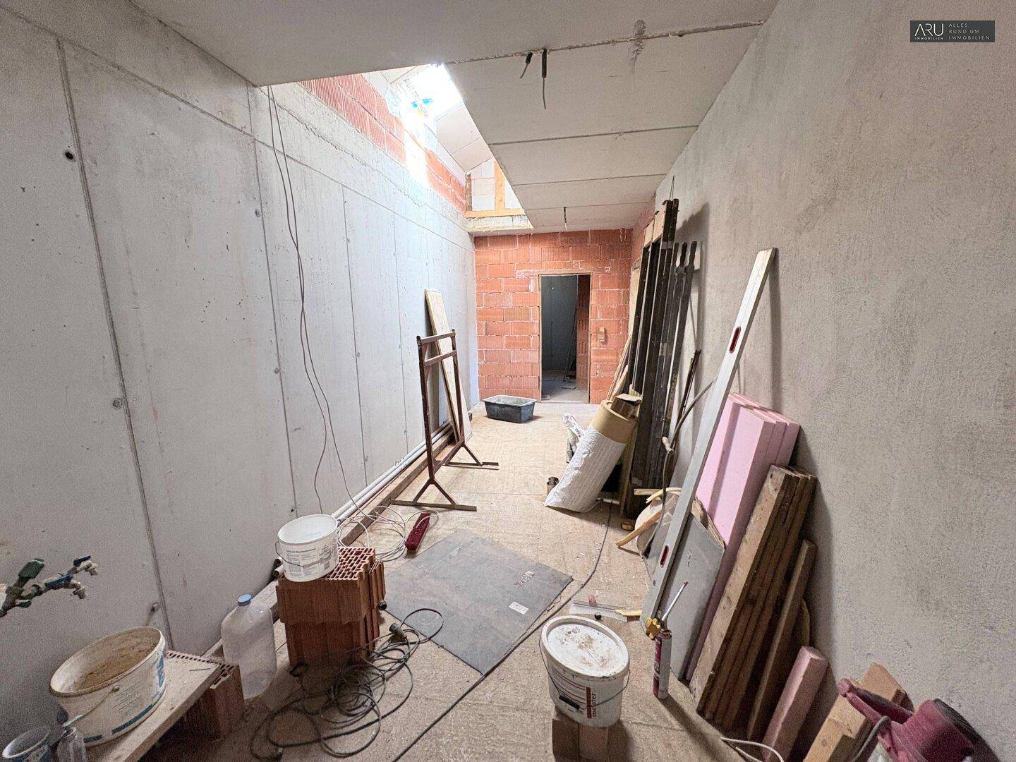 Unfertiger Flur mit Ziegelwänden, Betonboden und Baumaterialien, bereit für den Ausbau.
