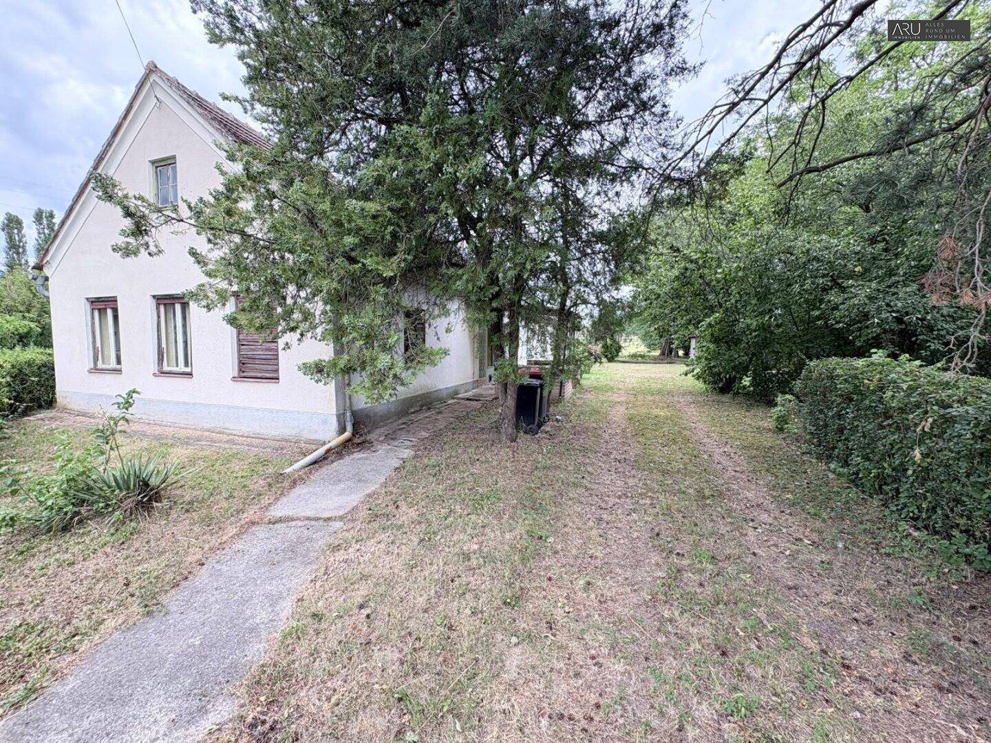 Seitenansicht des Hauses mit Zufahrt und Bäumen im ländlichen Umfeld.