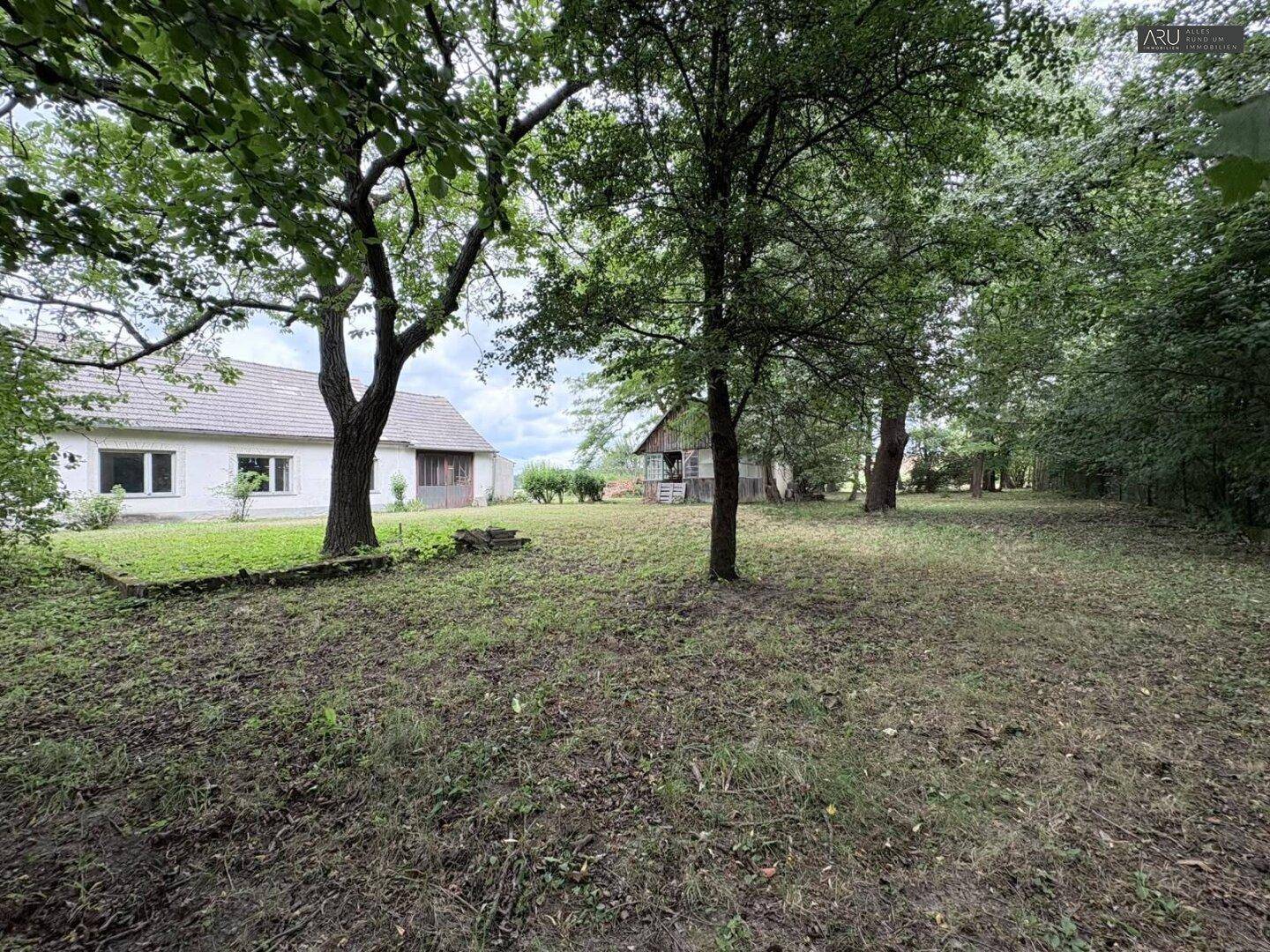 Großer Garten mit Rasen, Bäumen und Blick auf das Haupthaus sowie ein Nebengebäude.