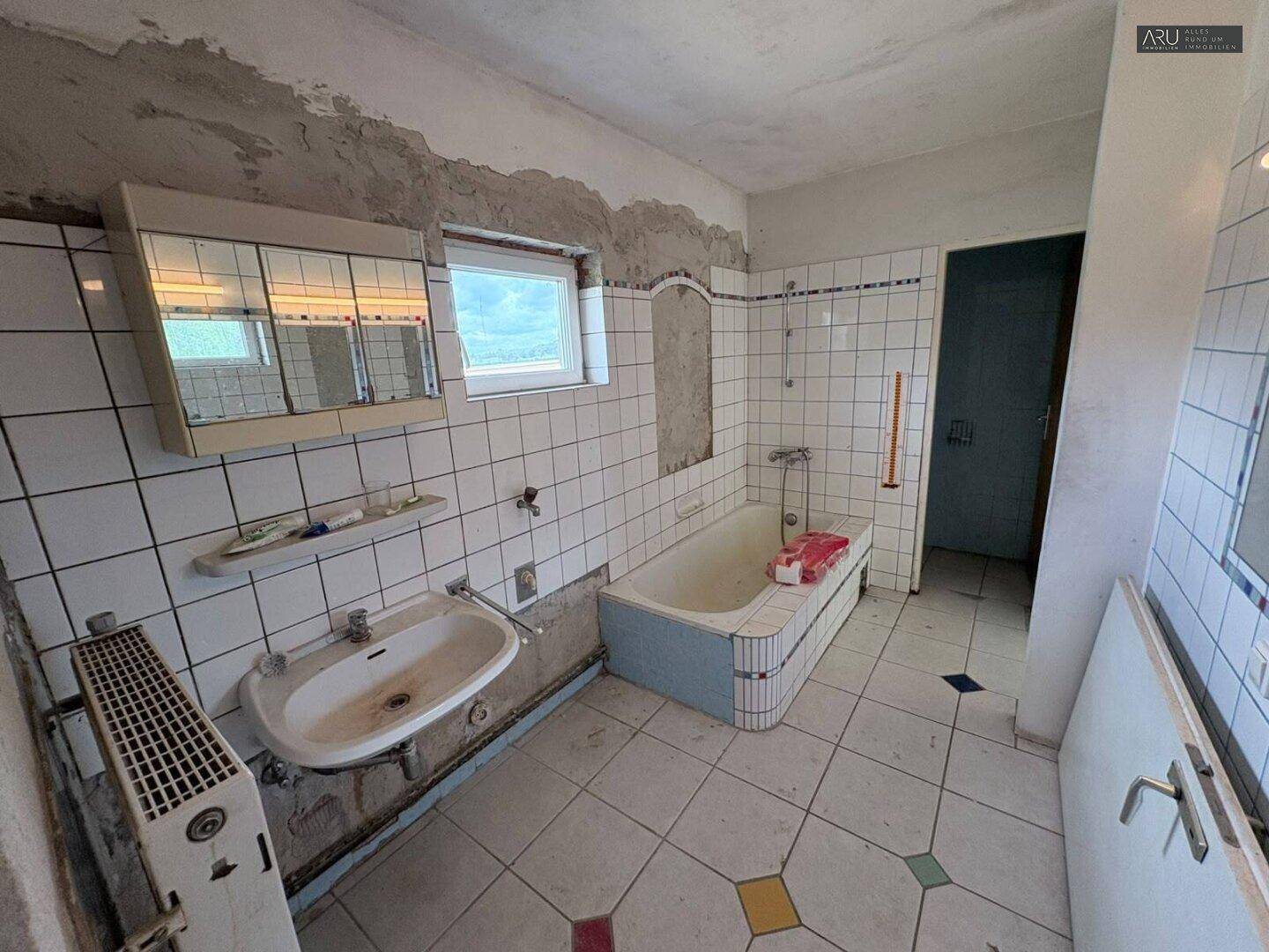 Renovierungsbedürftiges Badezimmer mit Badewanne, Waschbecken und Fliesen aus den 80er Jahren.