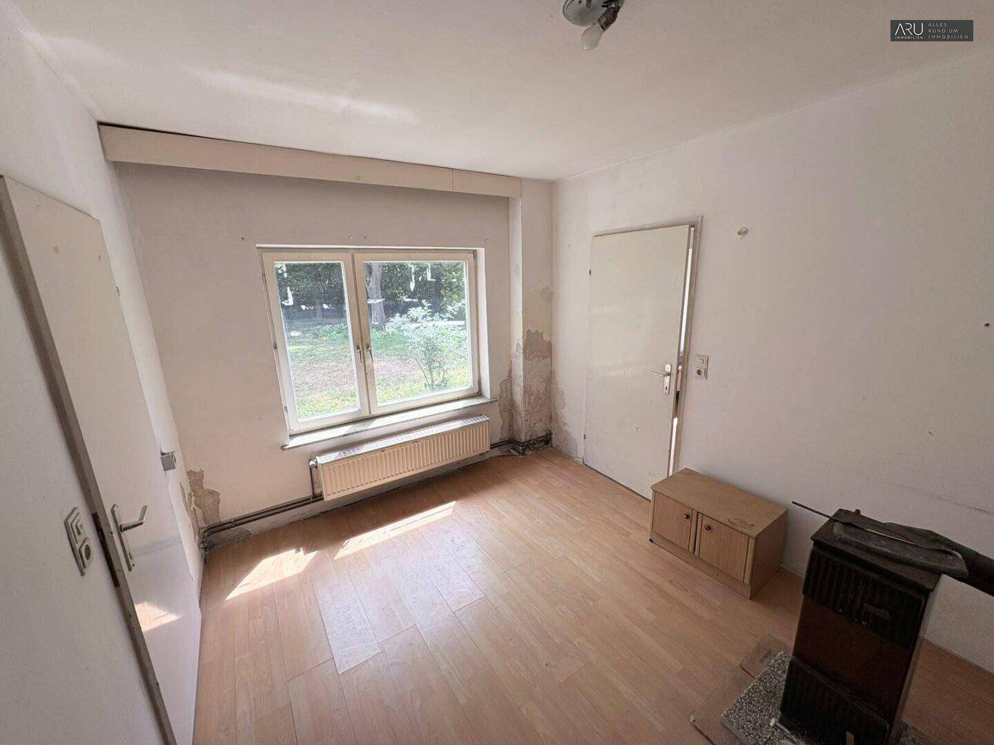 Kleiner Raum mit hellem Laminatboden, Fenster und einem Holzofen.