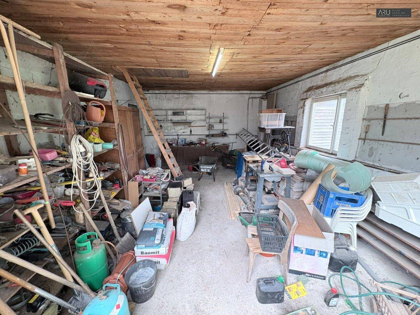 Unaufgeräumter Abstellraum oder Werkstatt mit Holzdecke und vielen Gegenständen.