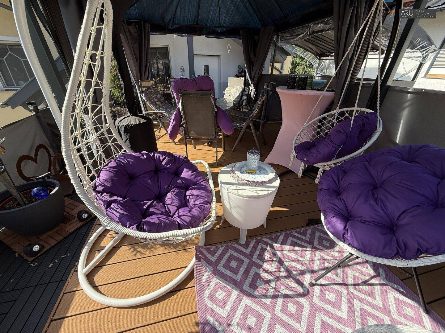 Gemütliche Terrasse mit Hängesesseln und lila Kissen für entspannte Stunden.