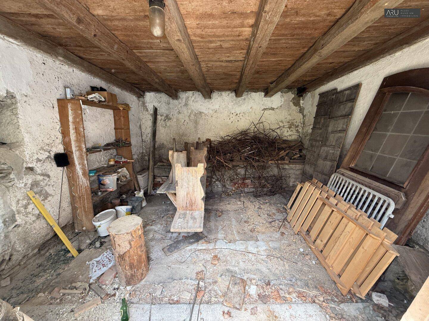 Unfertiger Raum mit Holzbalkendecke, Schutt und alten Türen, die auf eine Renovierung warten.